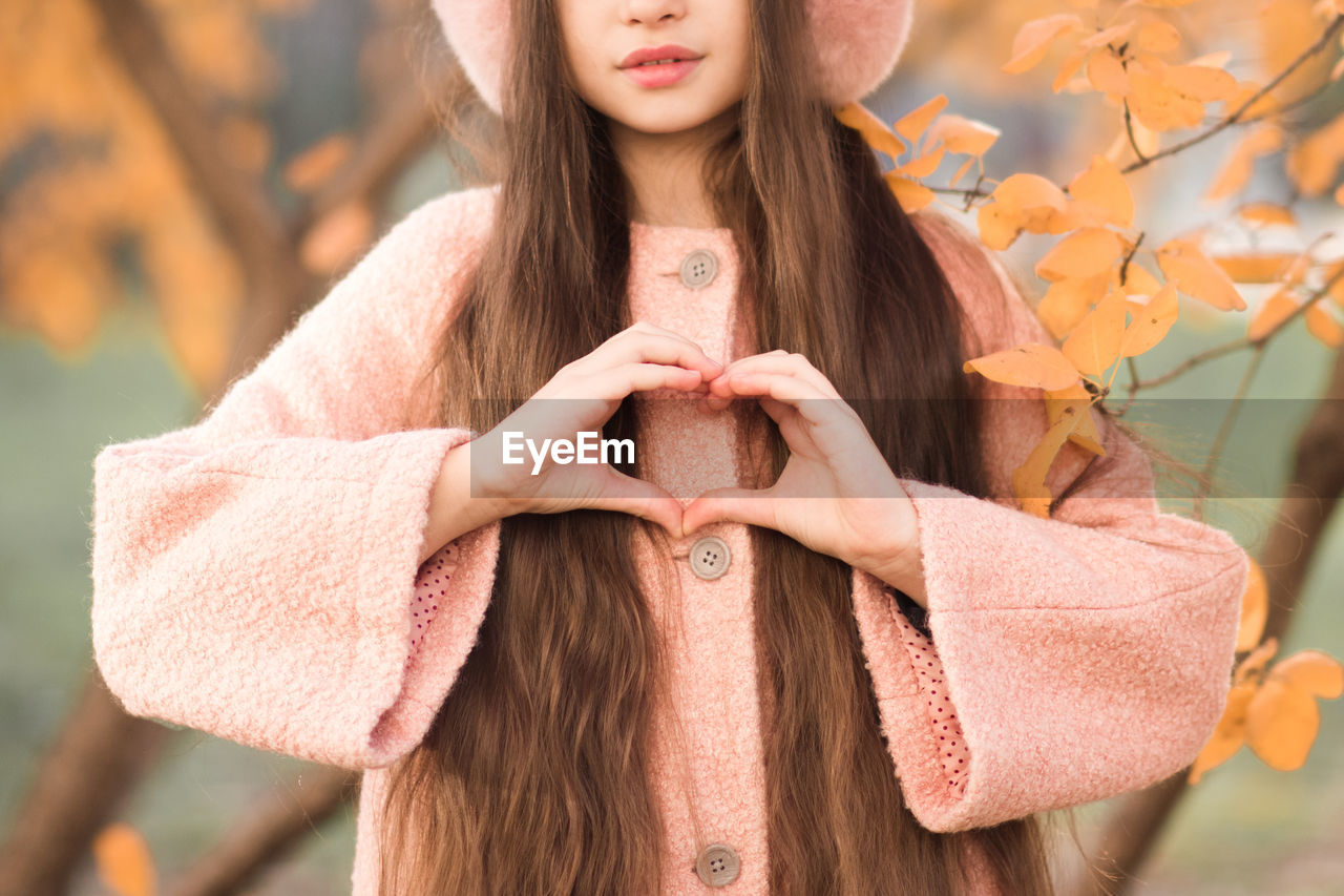 Portrait of kid girl 10-12 year old with long hair wear casual jacket make heart shape with hand