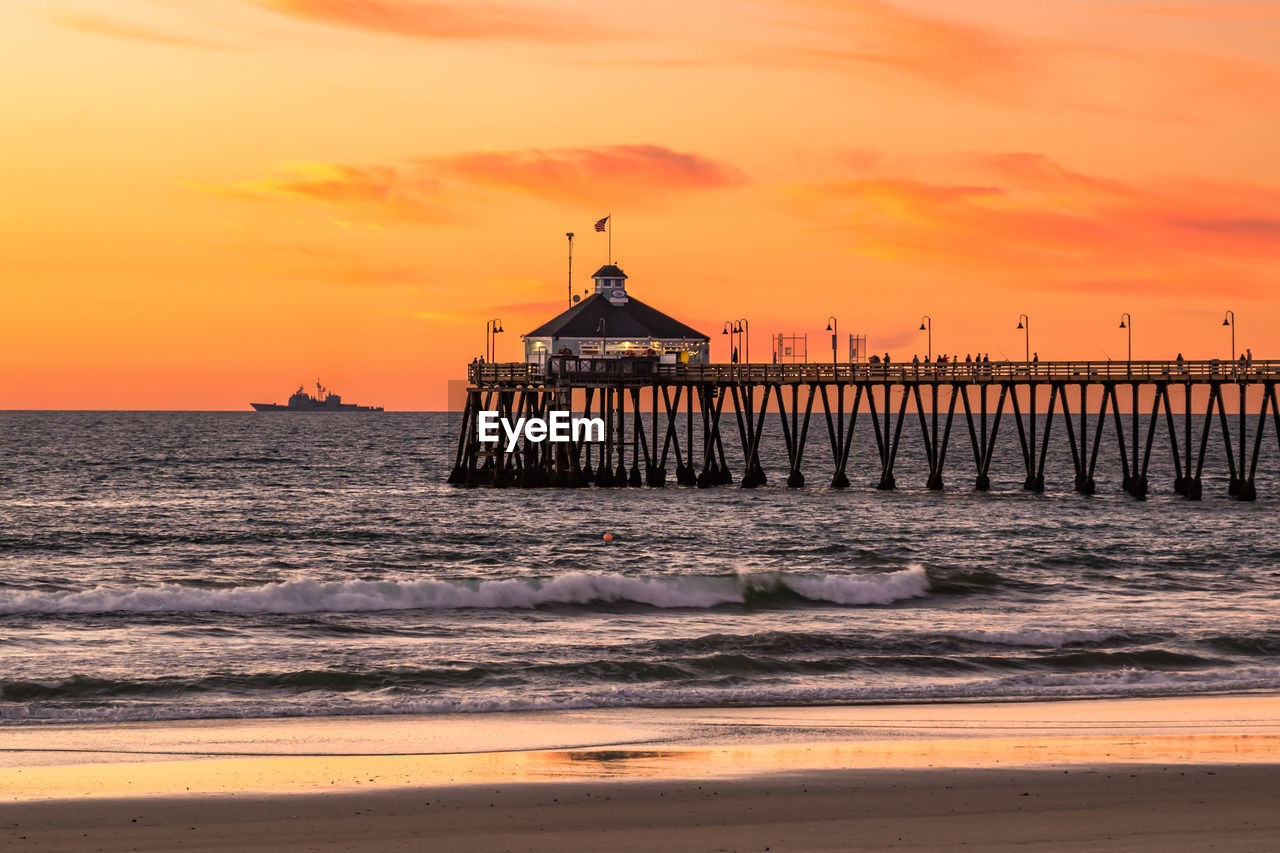 water, sea, sunset, sky, pier, architecture, ocean, beach, land, built structure, shore, coast, horizon, nature, wave, beauty in nature, travel destinations, orange color, cloud, scenics - nature, dawn, building exterior, horizon over water, sand, body of water, travel, building, evening, no people, motion, sun, afterglow, tranquility, tourism, outdoors, tower, wood, idyllic, sunlight, tranquil scene, silhouette, history, dramatic sky, holiday, environment, the past, seascape