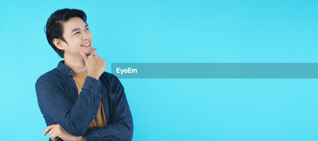 TEENAGE BOY LOOKING AWAY AGAINST BLUE BACKGROUND