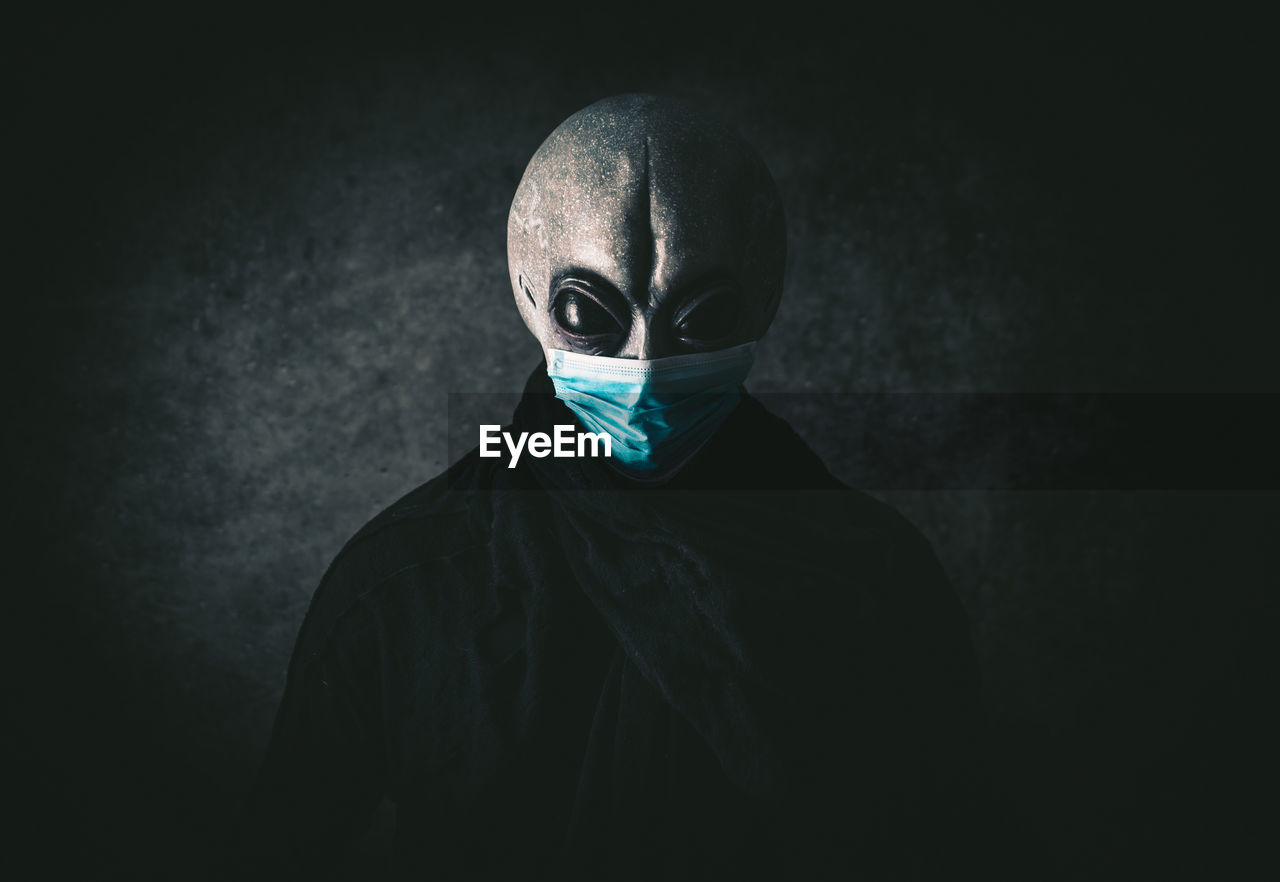 Portrait of alien wearing mask against black background