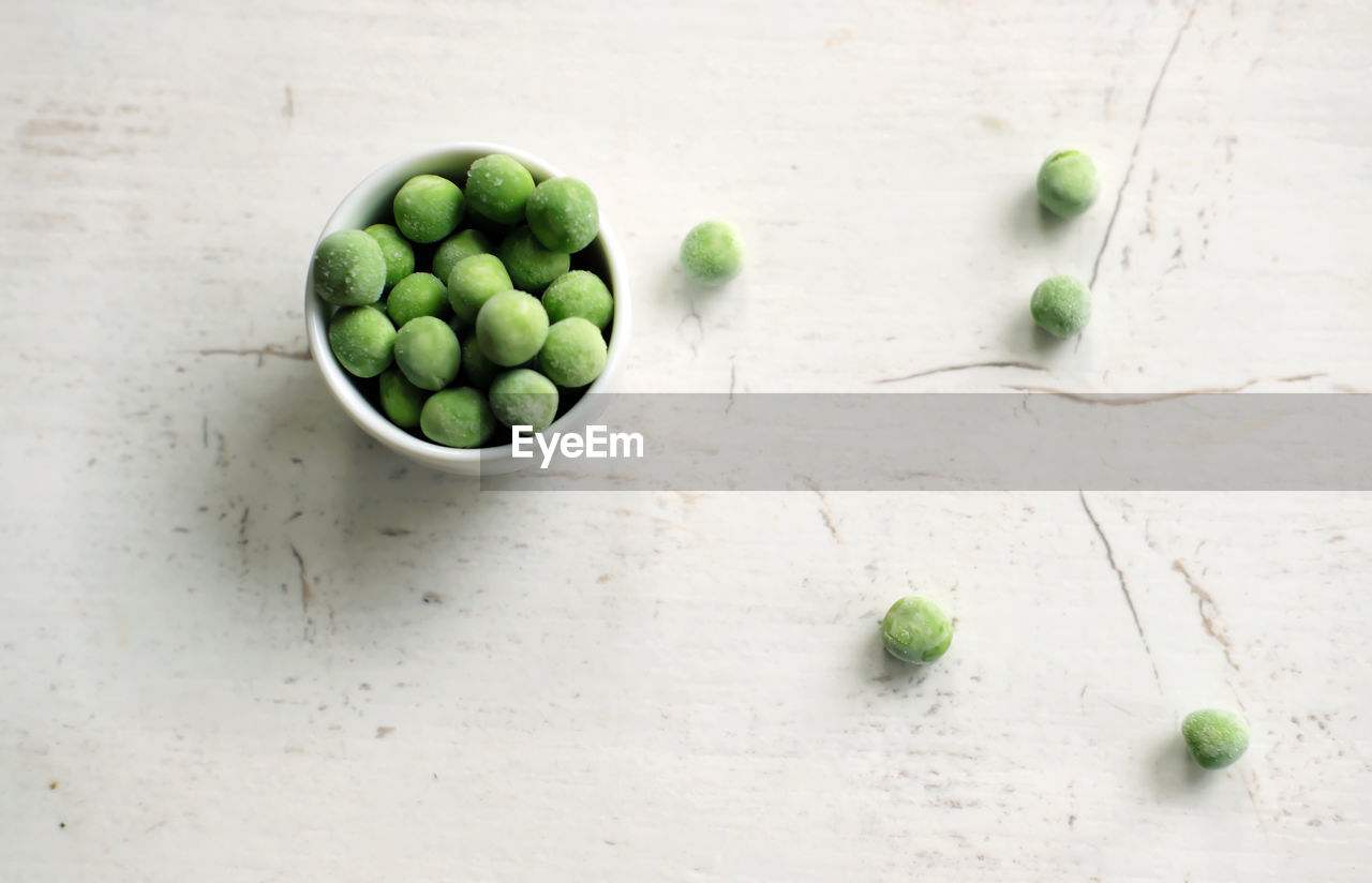 Frozen green peas in a bowl on white rustic wooden board - top view