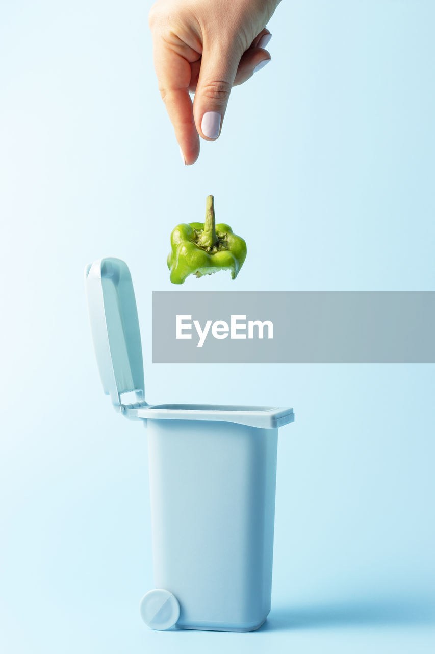 Female hand throws food trash into trash can on a blue background.