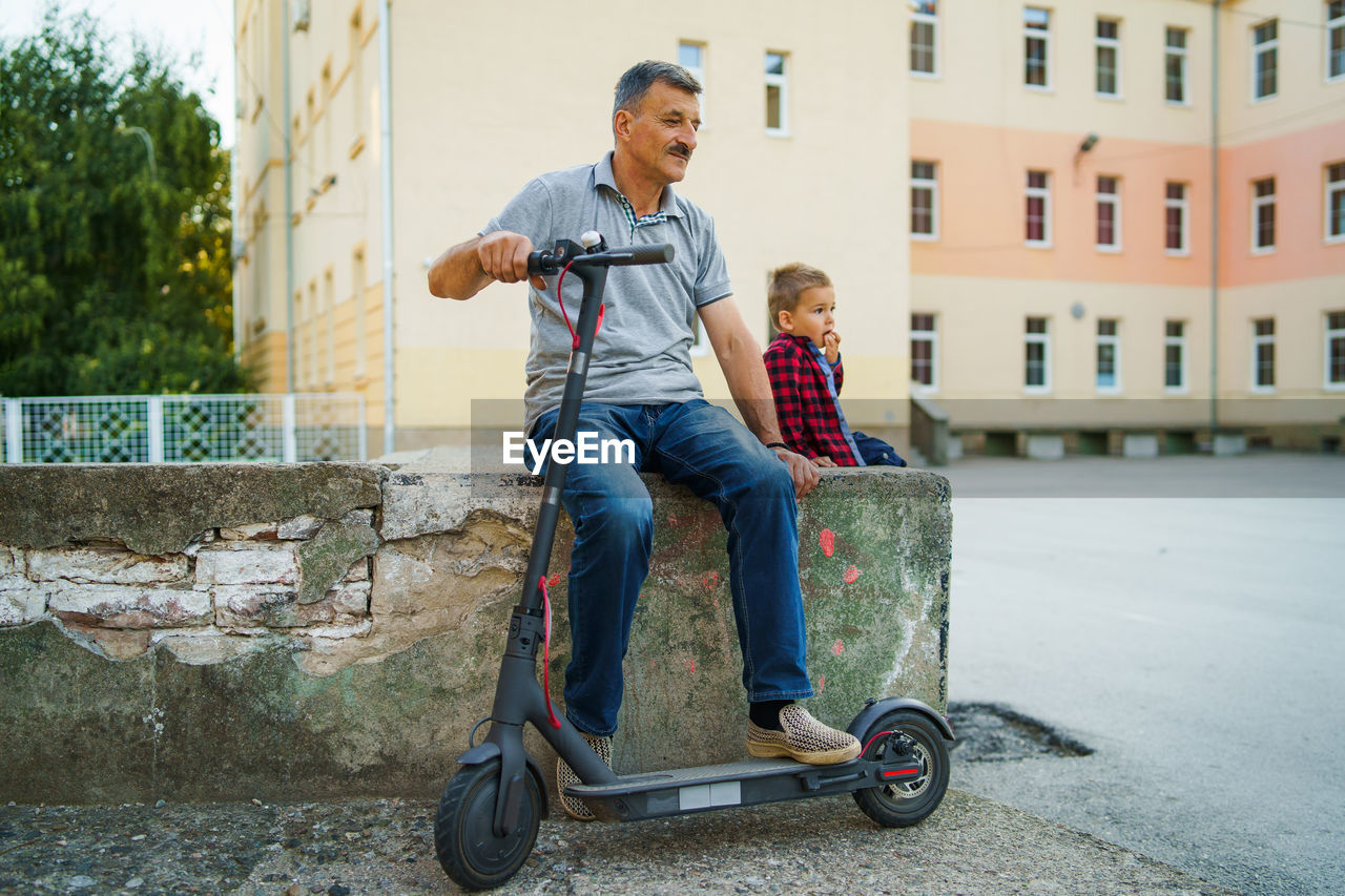 Father and son with push scooter sitting on retaining wall