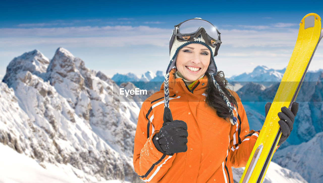 Portrait of cheerful woman holding skis while standing against snowcapped mountains