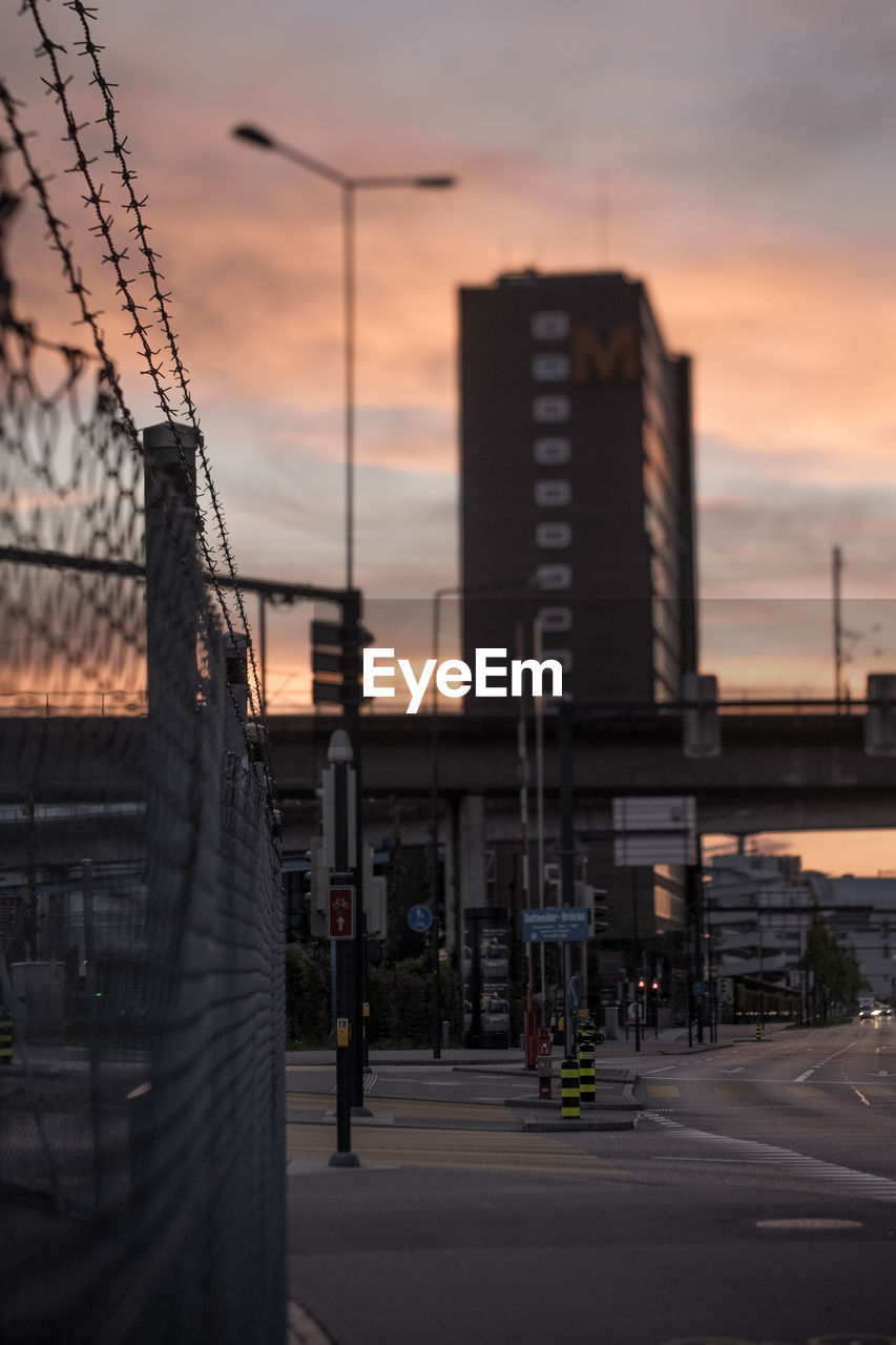 CITY STREET BY BUILDINGS AGAINST SKY AT SUNSET