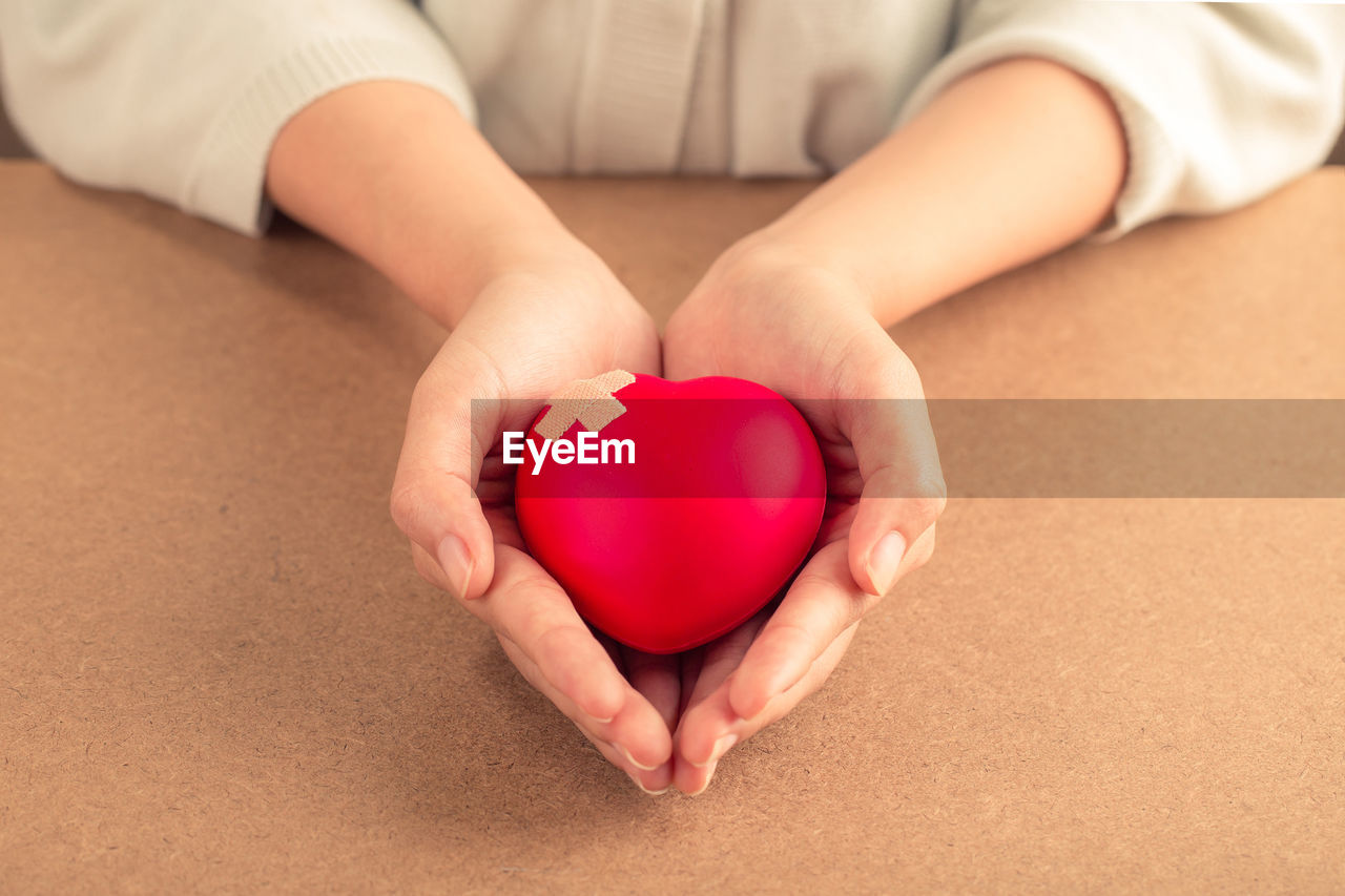 Woman holding red heart with bandage on wooden background. health care concept.world heart day