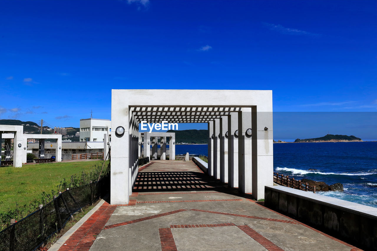 Walkway by sea against clear blue sky