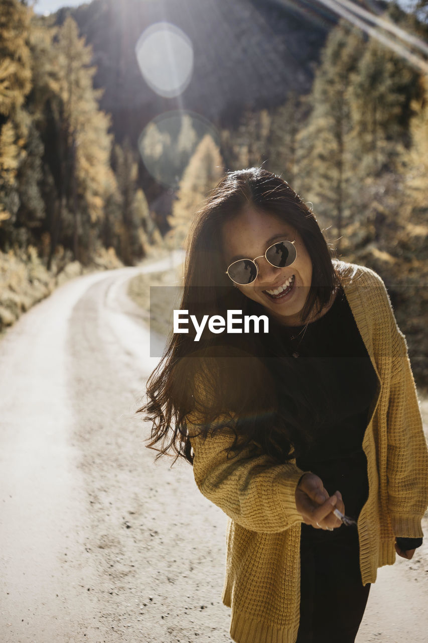 Young woman wearing sunglasses holding cigarette while standing against forest path