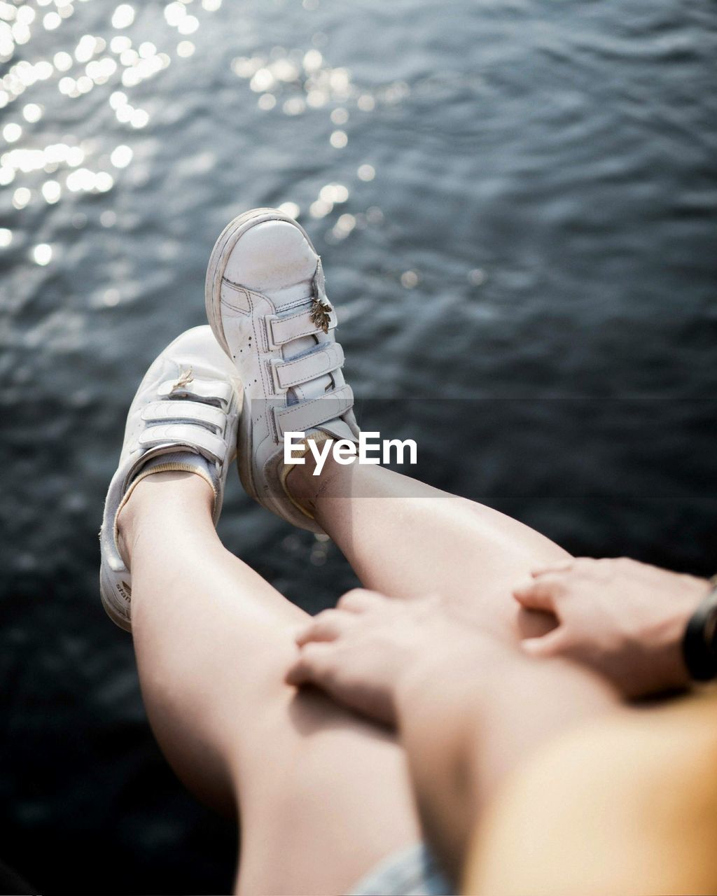 LOW SECTION OF WOMAN SITTING AGAINST LAKE