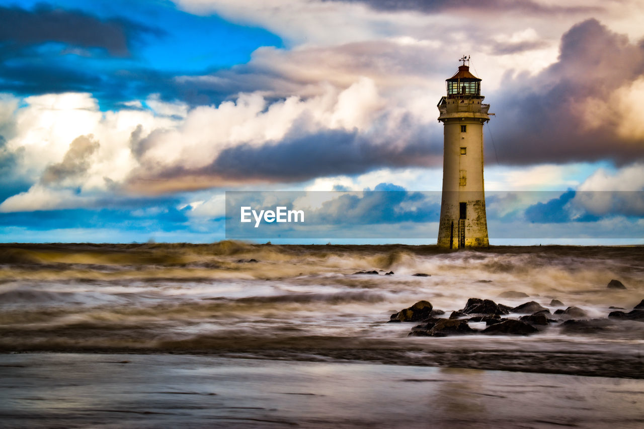 Lighthouse on beach by sea against sky