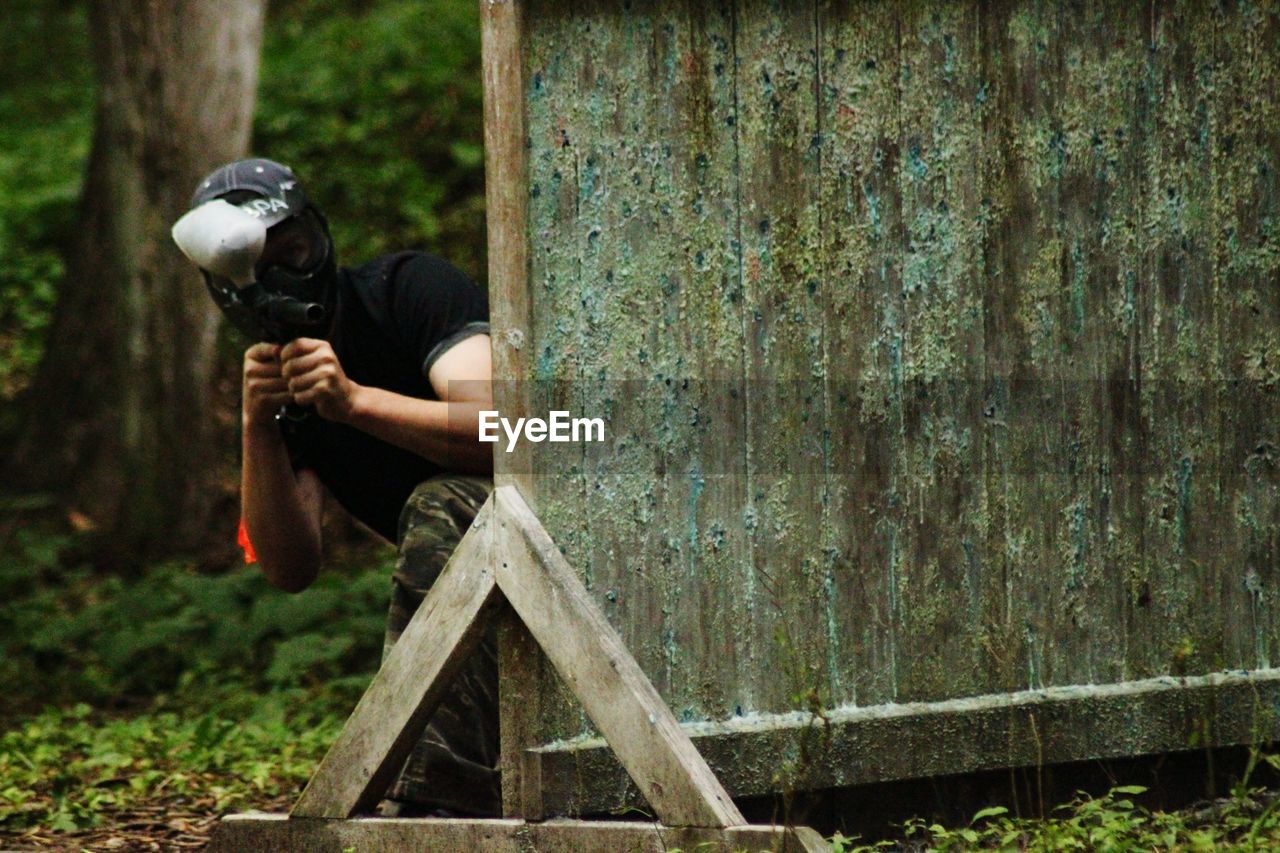 Man wearing mask while kneeling by wood in forest