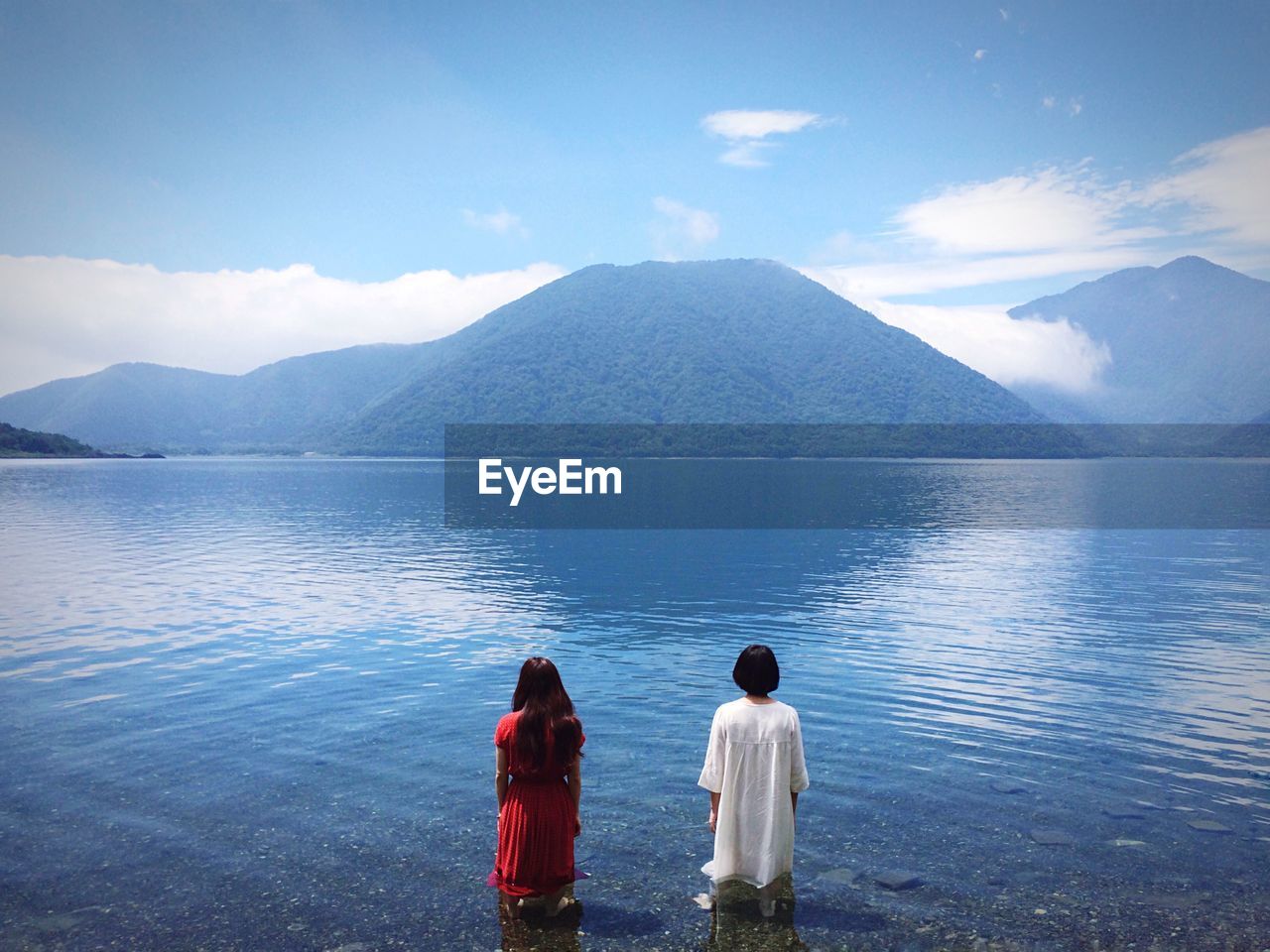 Two women standing in lake in front on mountains