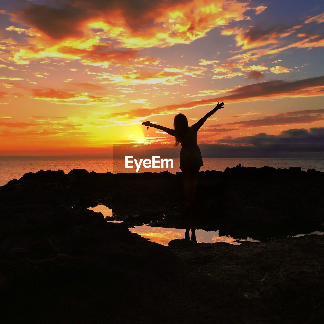 Silhouette woman with arms outstretched standing on beach at sunset