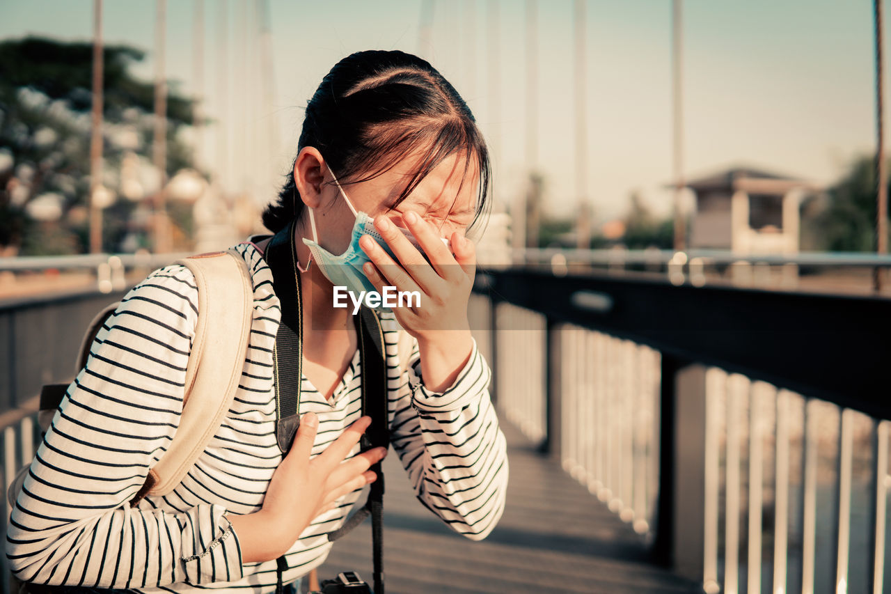 MIDSECTION OF WOMAN STANDING ON RAILING AGAINST BRIDGE