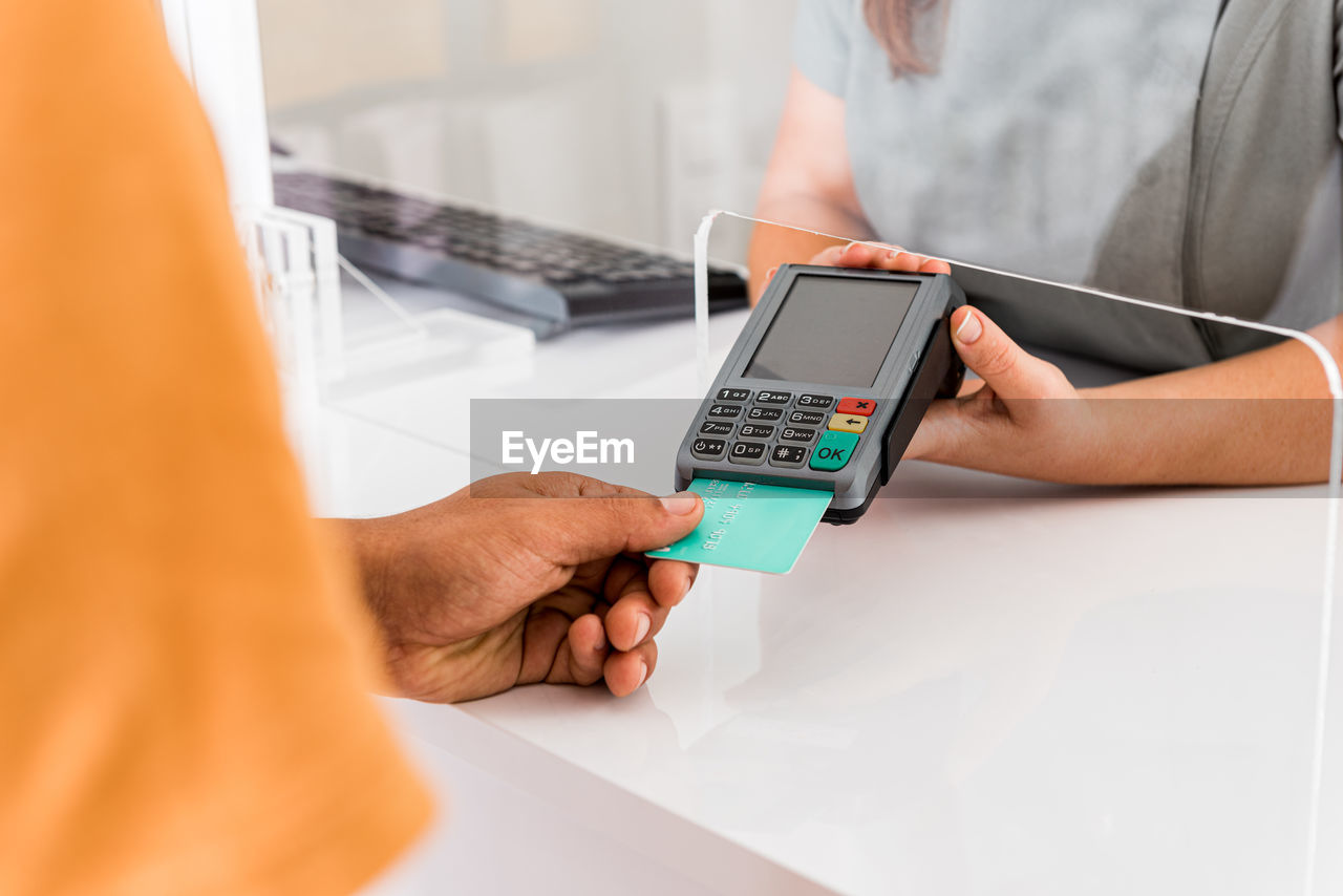 Cropped unrecognizable female specialist holding card reader while male patient paying for treatment with credit card in modern clinic