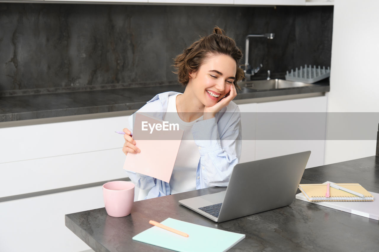 young woman using laptop while sitting on table in office