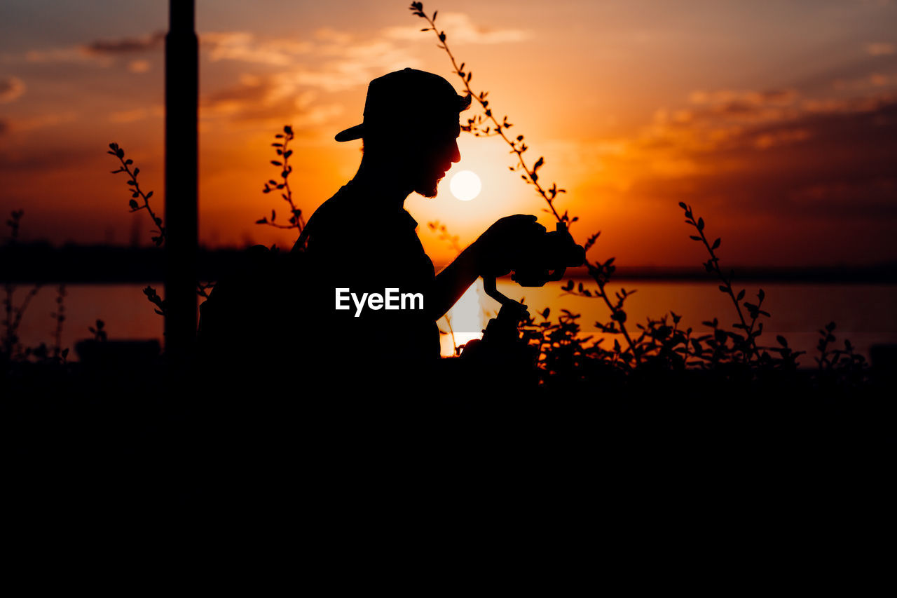 SILHOUETTE MAN STANDING BY LAKE AGAINST SKY AT SUNSET