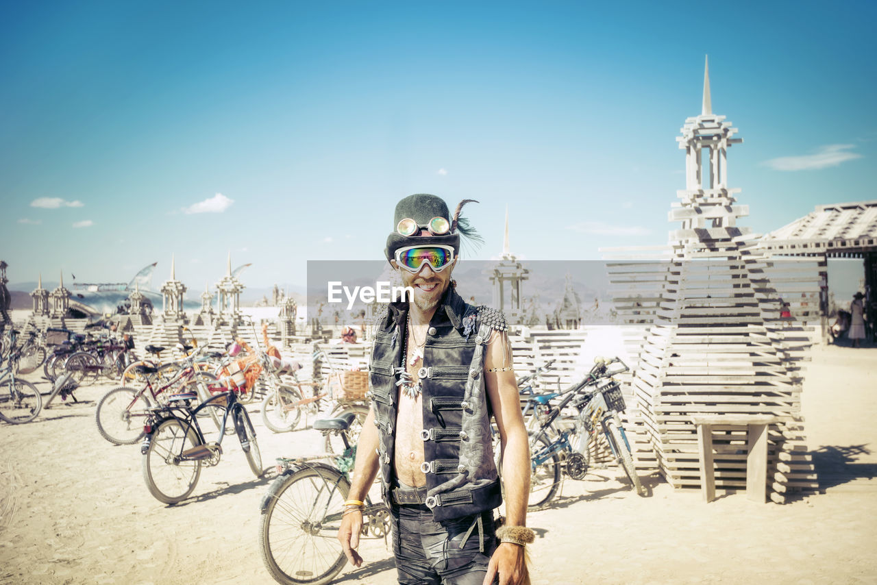 PORTRAIT OF MAN WITH BICYCLE STANDING AGAINST SKY IN CITY