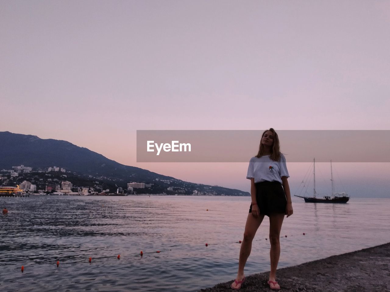 Full length of woman standing in seashore against sky during sunset