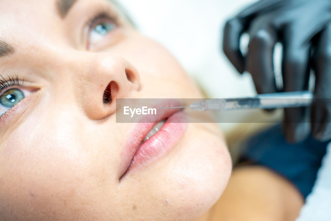 Cropped hand of cosmetician injecting fillers in woman lips