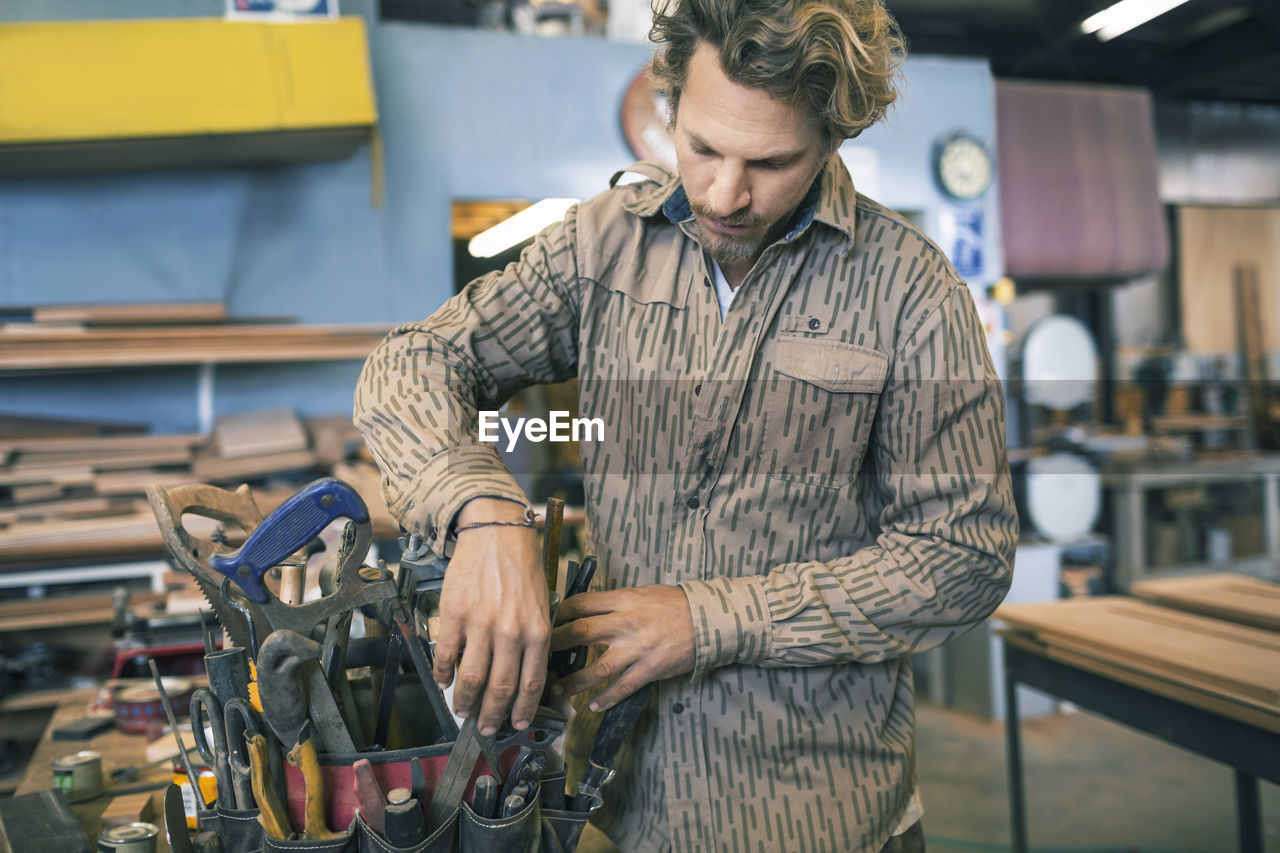 Carpenter arranging tools in belt at workshop