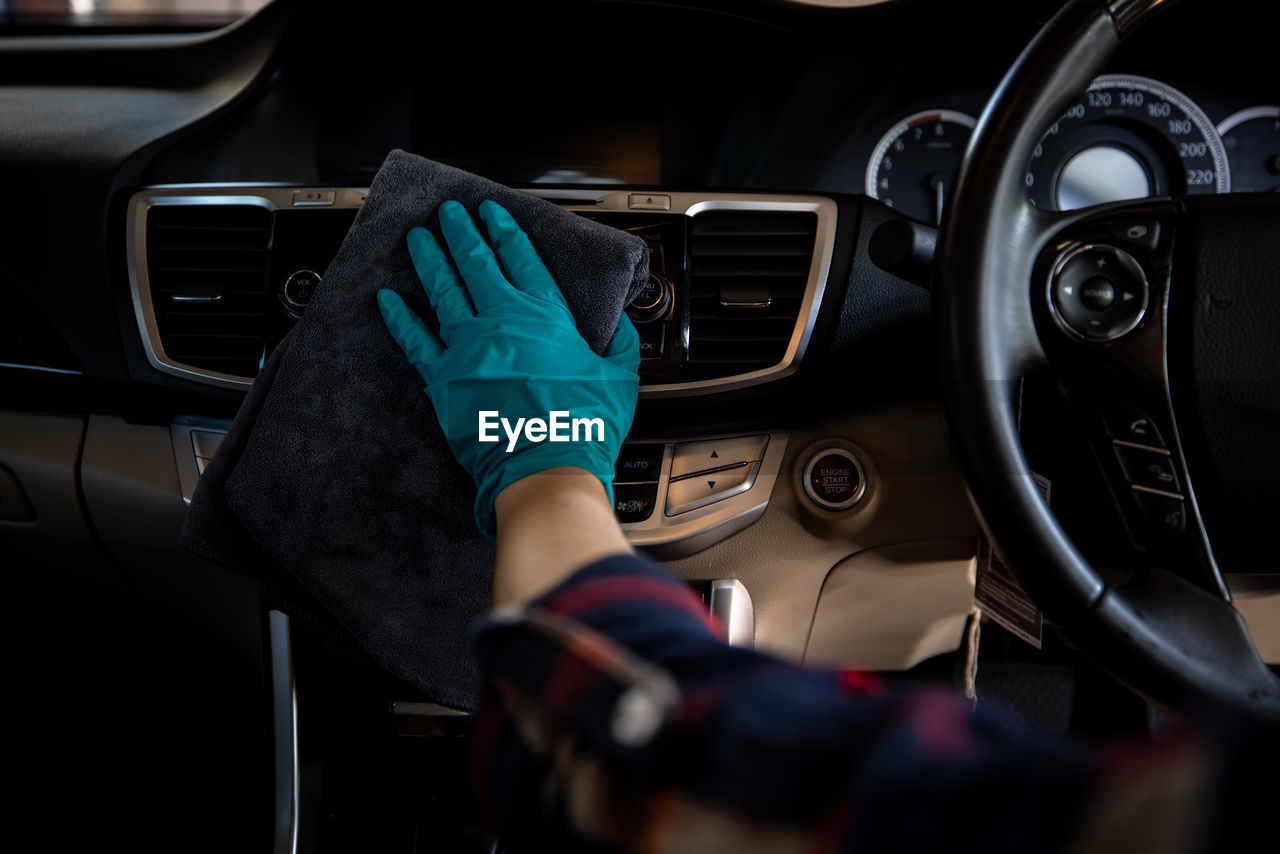 Worker women wear green gloves cleaning car interior console and air vent with gray microfiber cloth