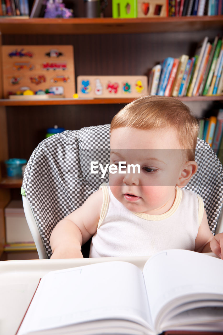 Cute baby boy with book on table at home