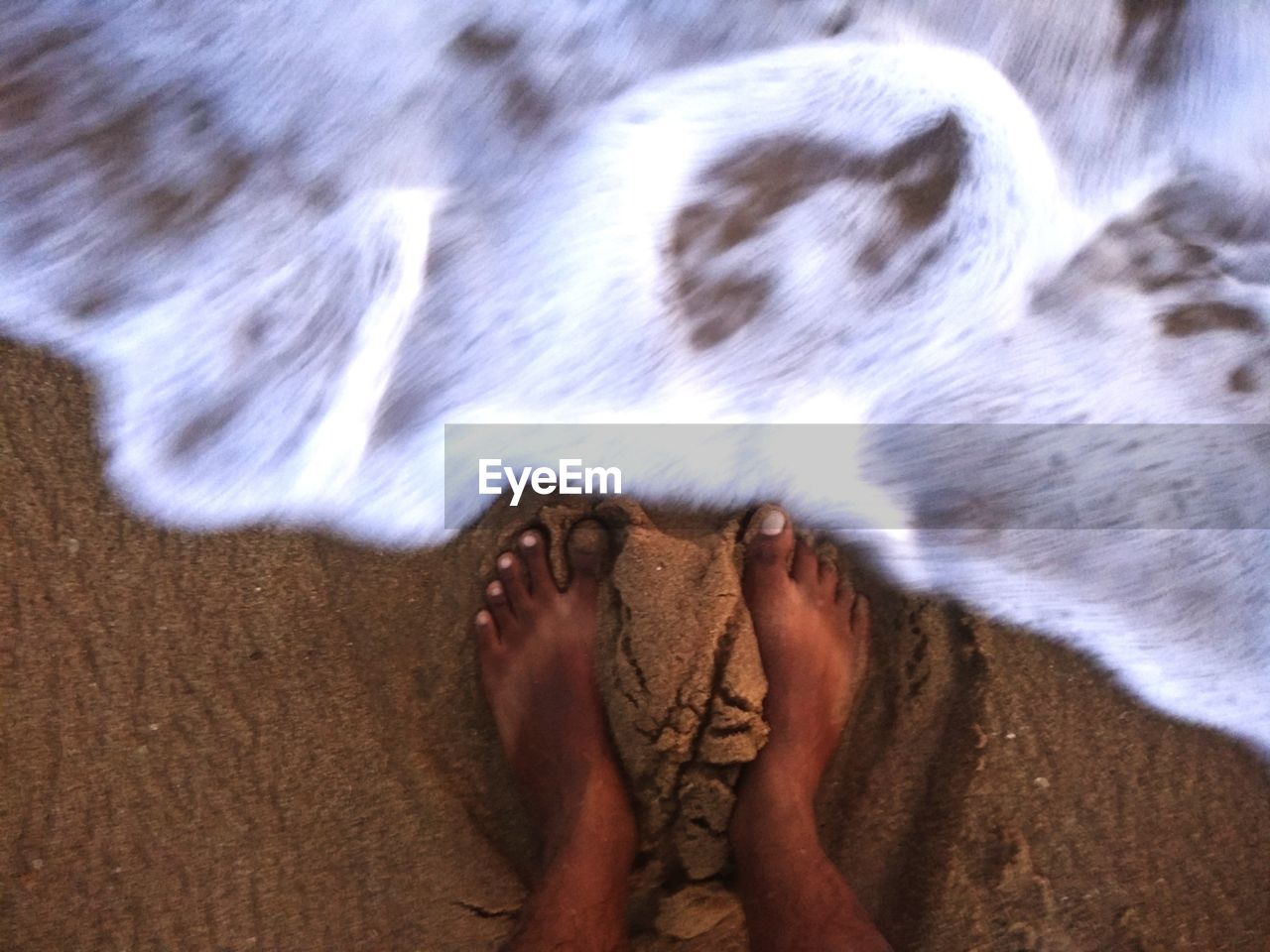 LOW SECTION OF PERSON STANDING ON SAND AT BEACH