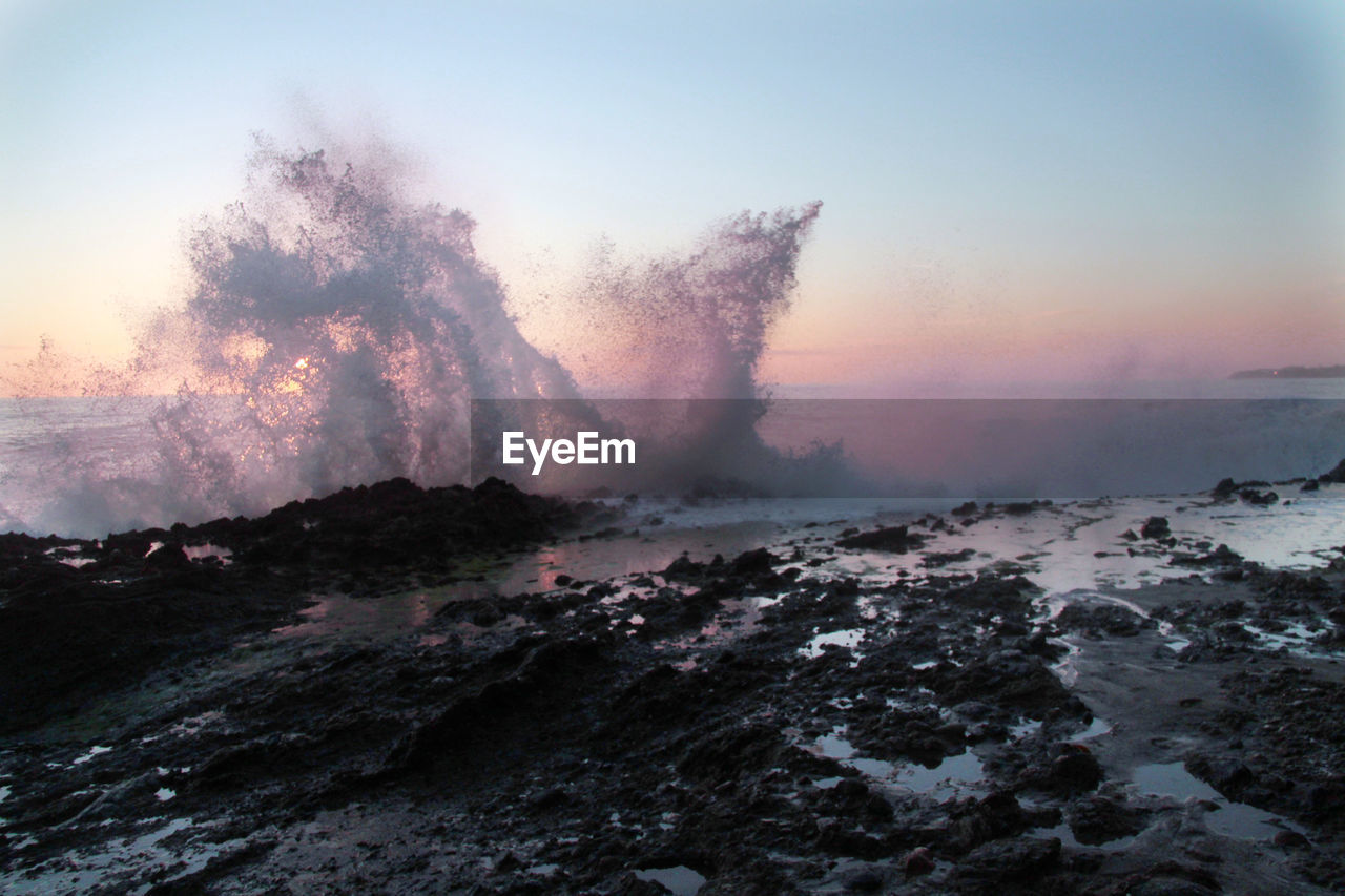 View of sea waves splashing at shore against sky during dusk