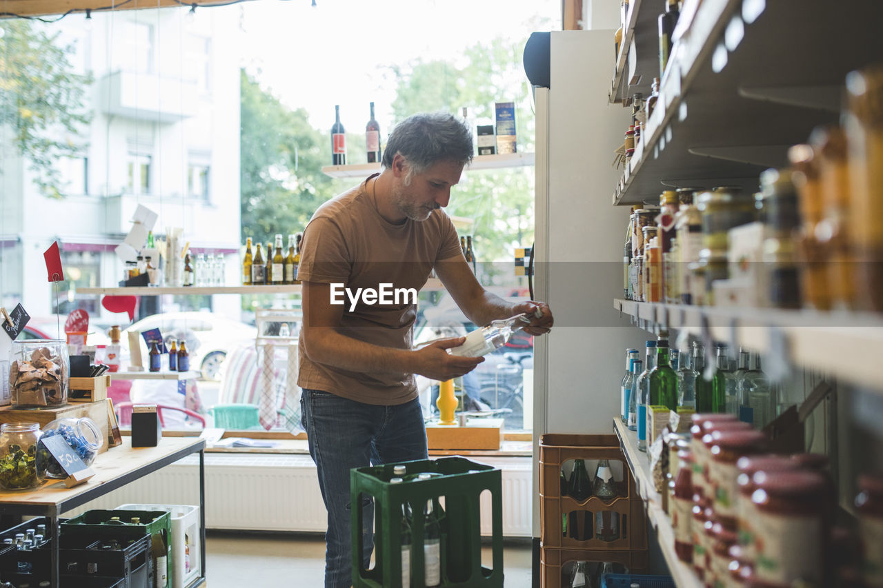Salesman arranging bottle on shelf in deli