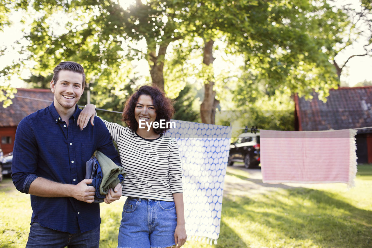 Portrait of smiling friends standing against clothesline in backyard