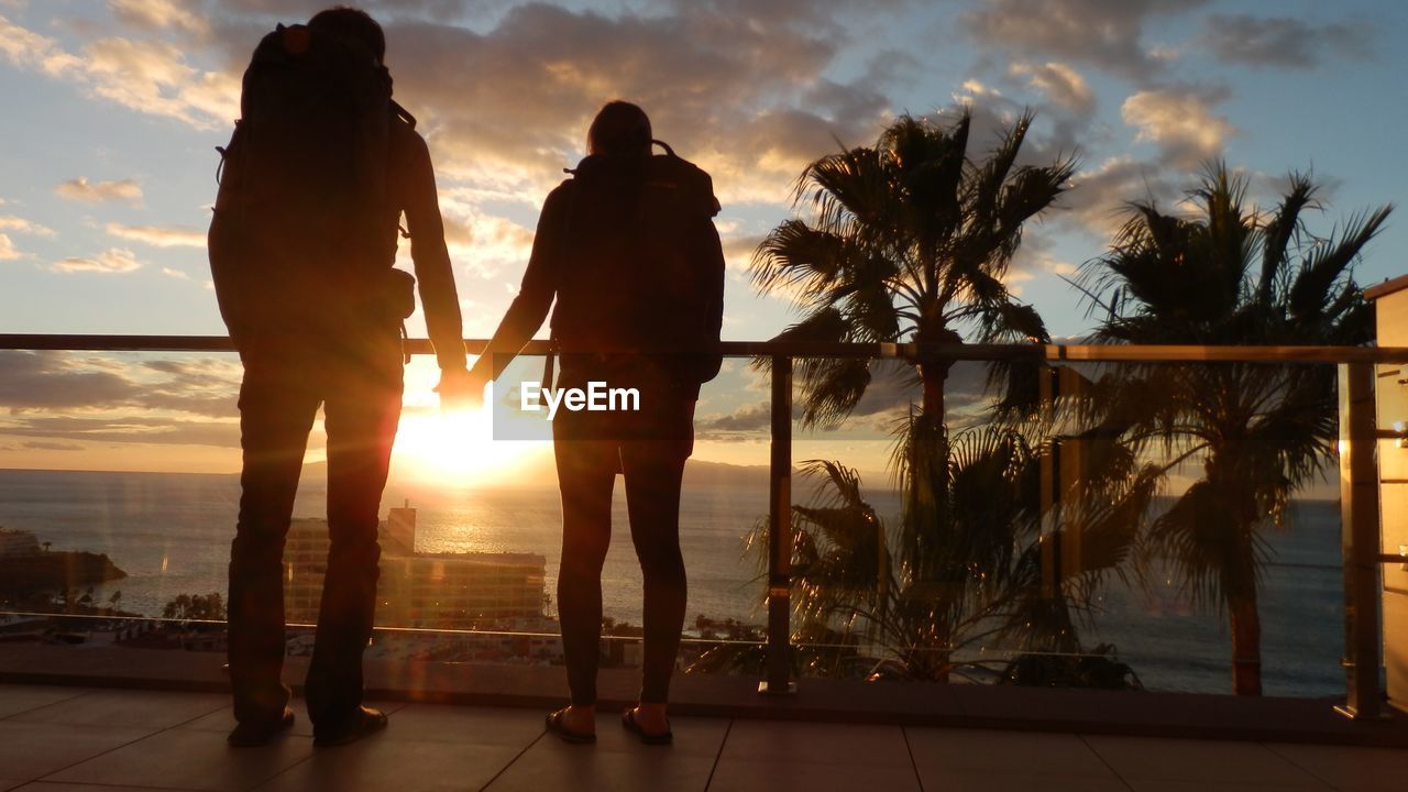 Rear view of silhouette hiking couple holding hands against sky during sunset