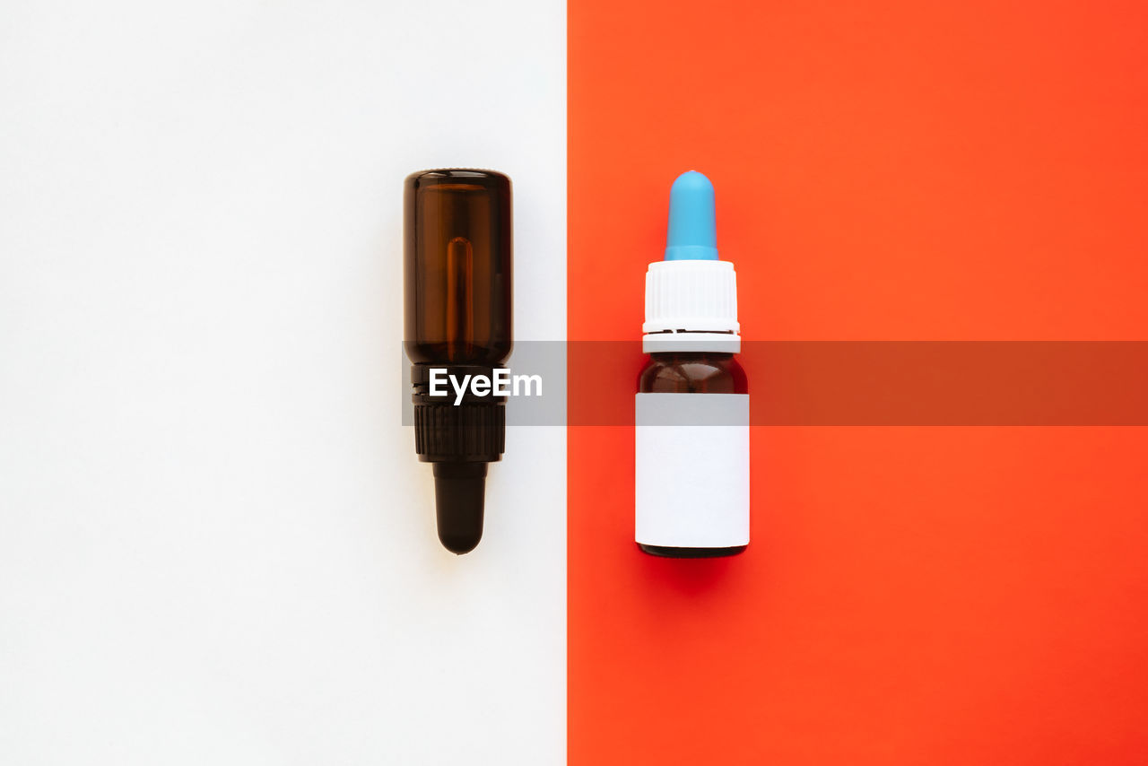 Two bottles with dropper against vibrant white and red backdrop. 