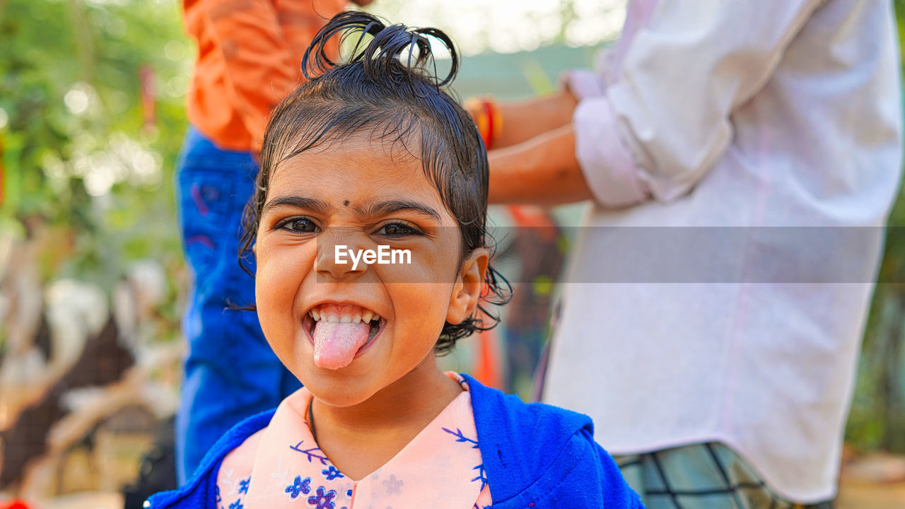 Close up portrait, asian little girl shows off her tongue. curly modern hairstyle with blue jacket.