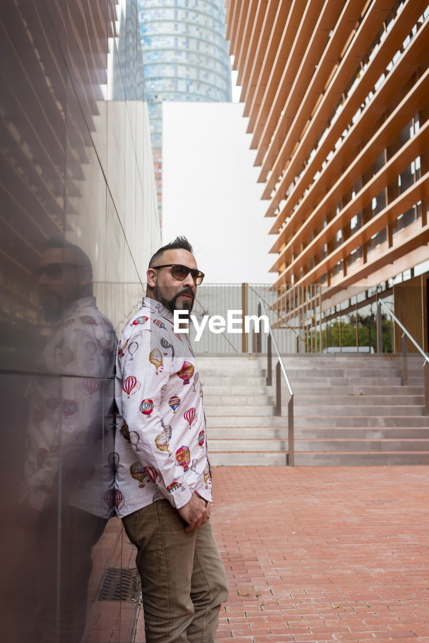 Side view of a bearded male leaning on a office building wall