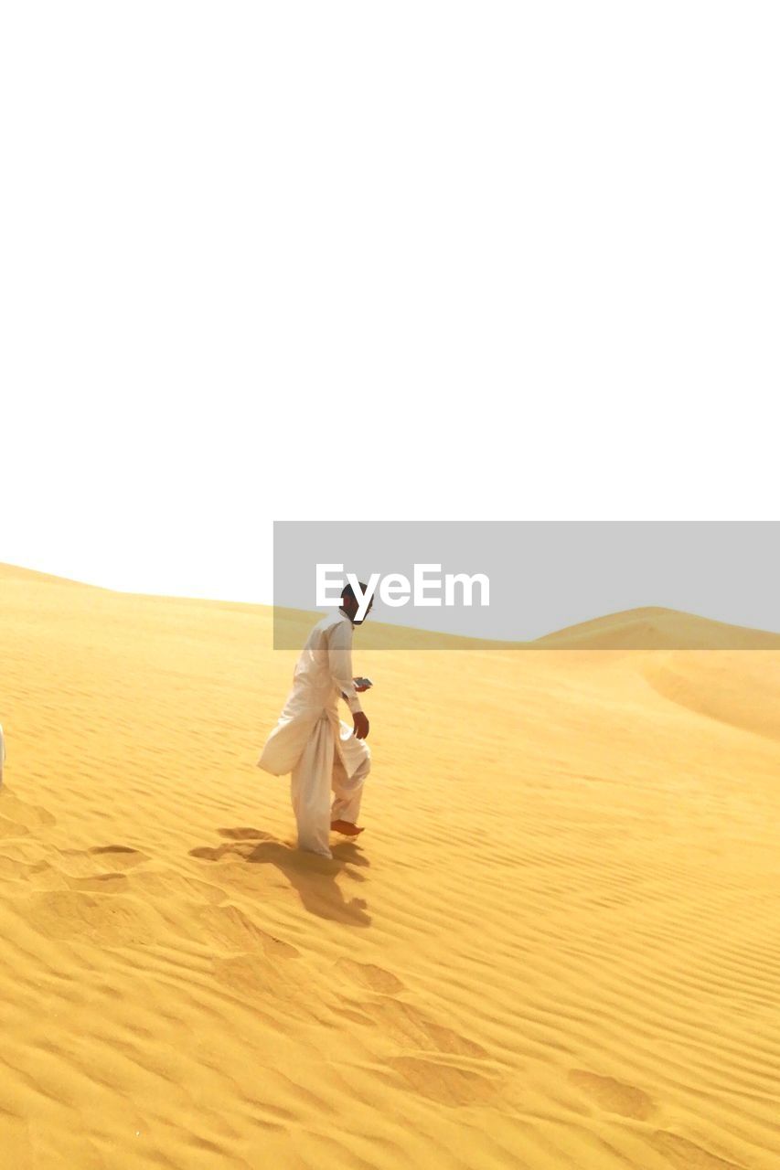 Full length of man walking on sand against clear sky