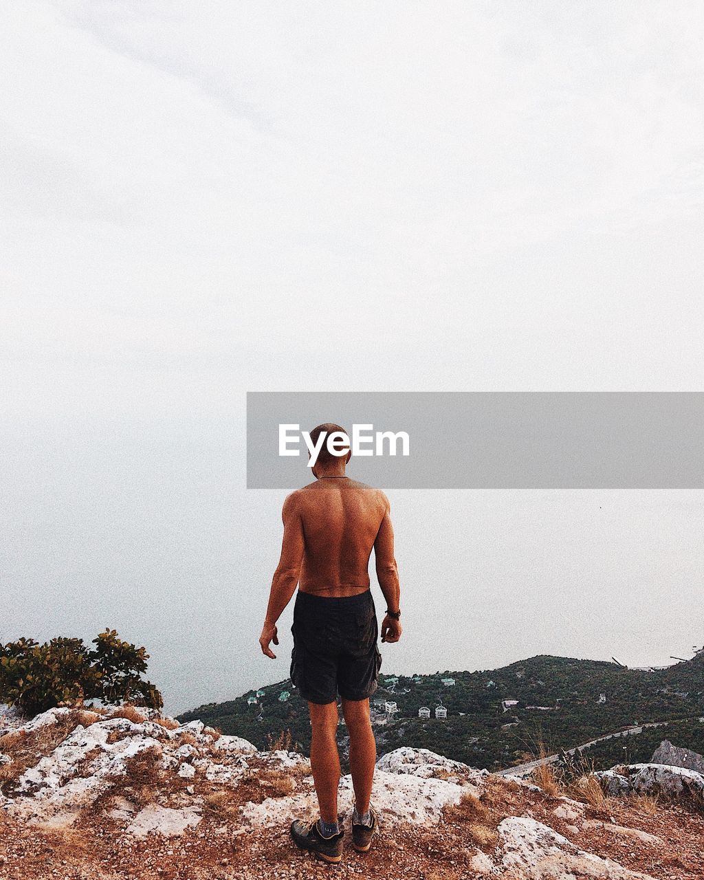 FULL LENGTH REAR VIEW OF SHIRTLESS MAN STANDING ON ROCK