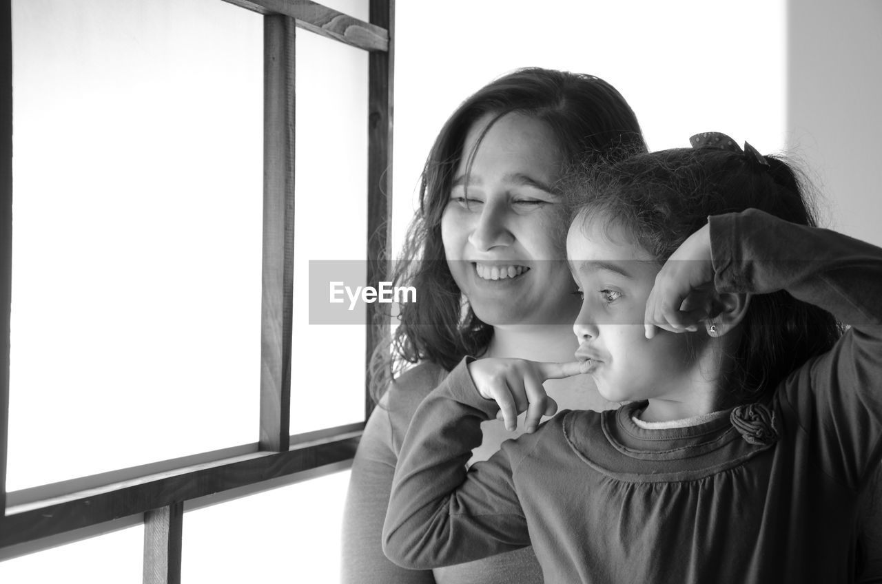 Smiling mother with daughter by window at home