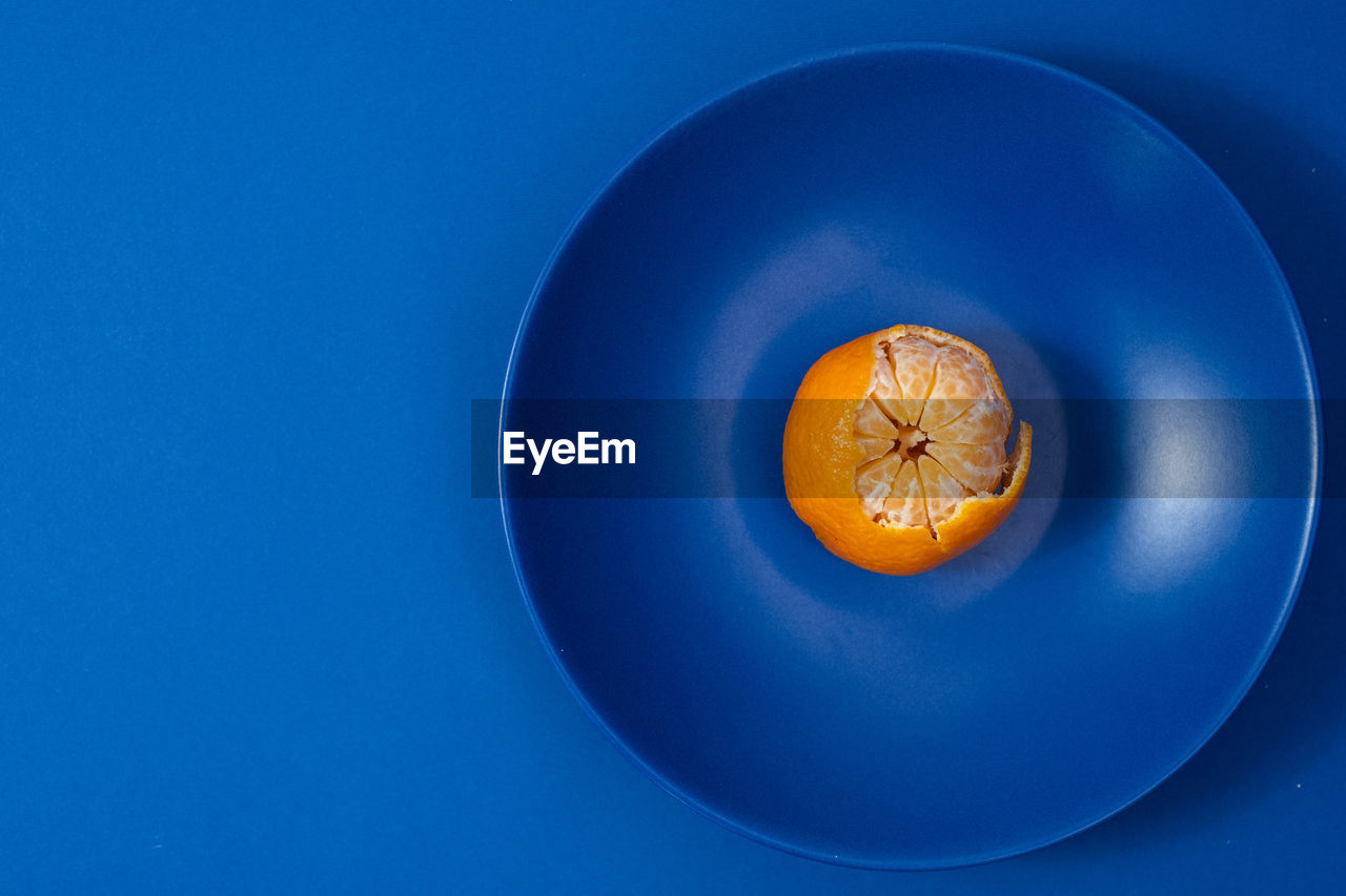 Half peeled tangerine on dark blue plate