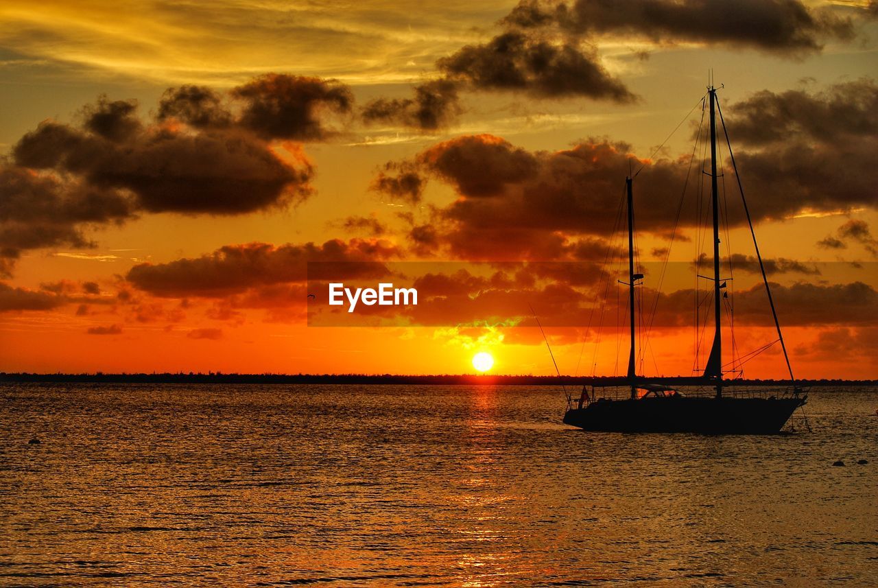 Boat sailing in sea against dramatic sky during sunset