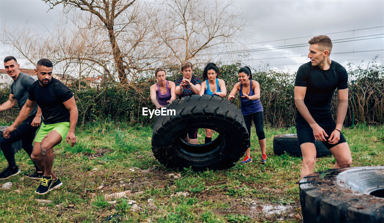 Friends pushing tire on field