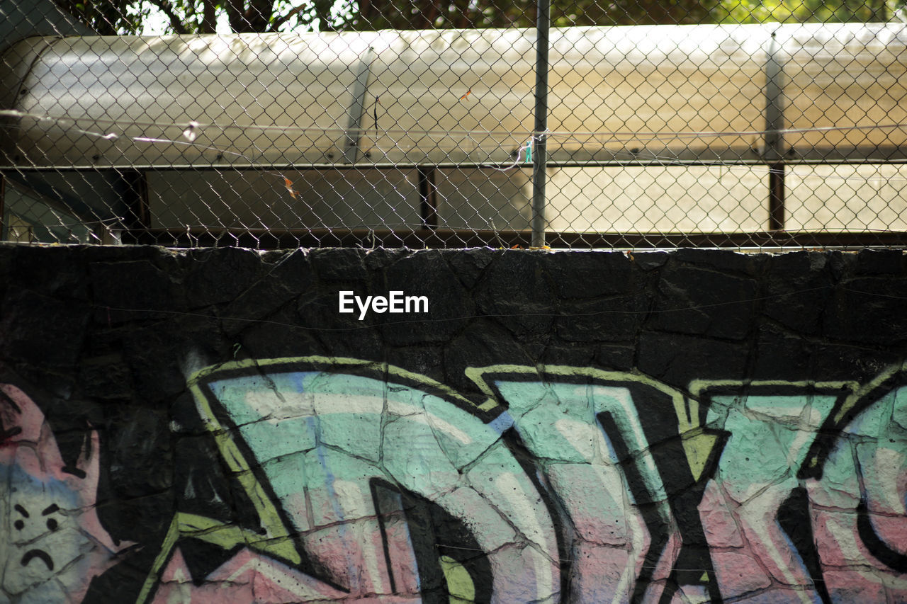 GRAFFITI ON CHAINLINK FENCE AGAINST ABANDONED BUILDING