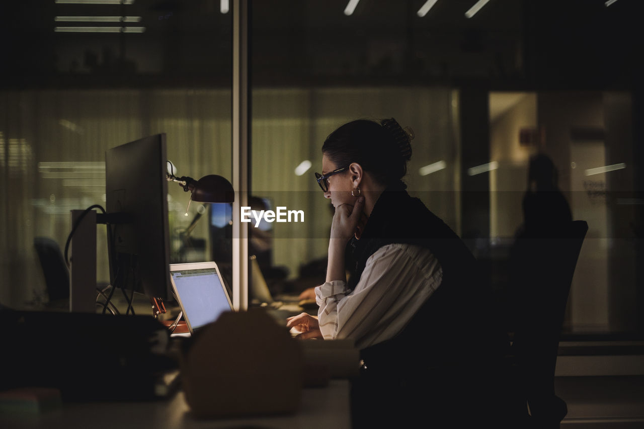 Ambitious businesswoman using laptop while working late in office at night