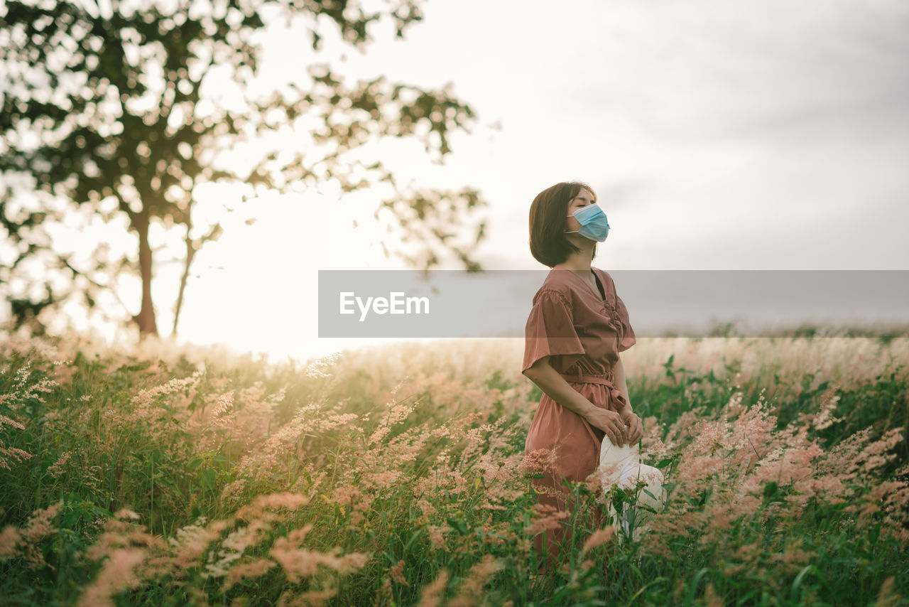 Girl on a spring meadow at sunset.  wears a dress and wide-brimmed hat. breathing through the mask.