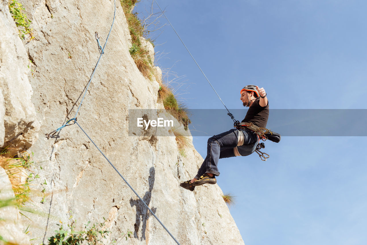 Sportive male alpinist climbing on sheer cliff in summer day