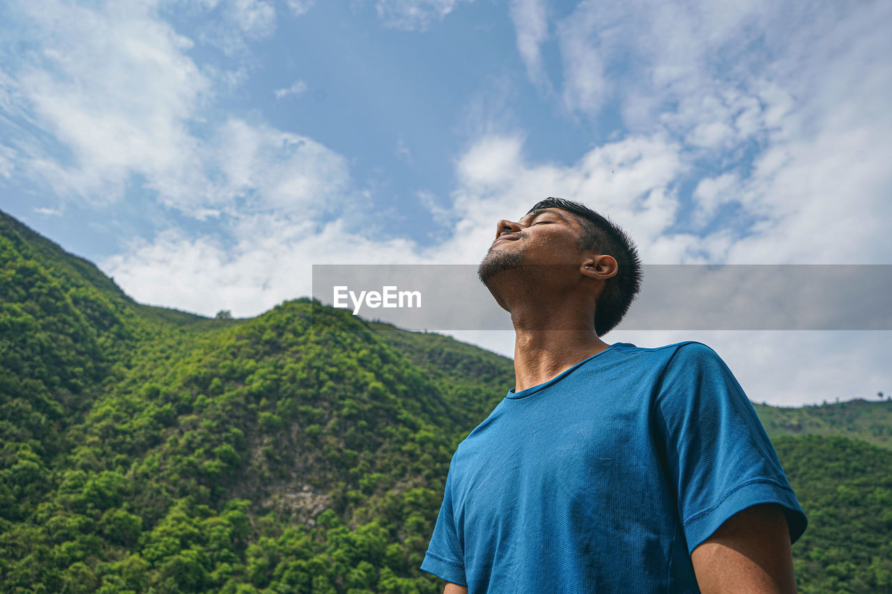 Young indian boy standing in the edge of the balcony, enjoying the scenic view of the green mountain