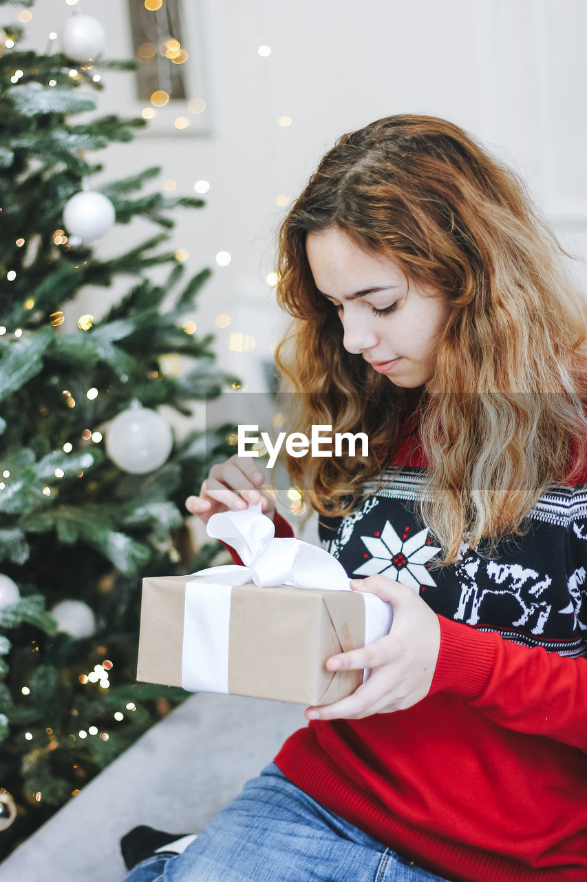 YOUNG WOMAN HOLDING CHRISTMAS TREE IN BOX ON TABLE