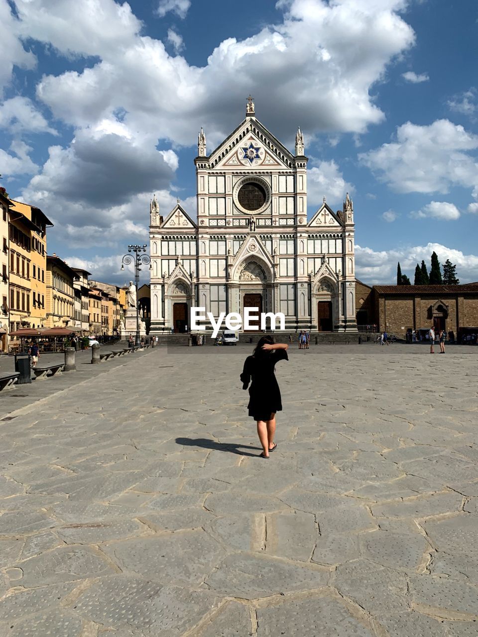 Rear view of woman walking towards church in city against cloudy sky