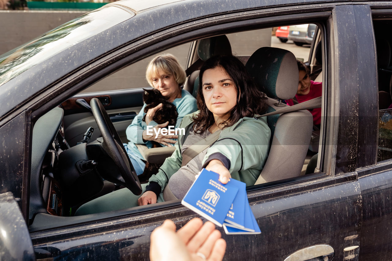 Family in car giving ukrainian passports for custom control crossing border  fleeing from war