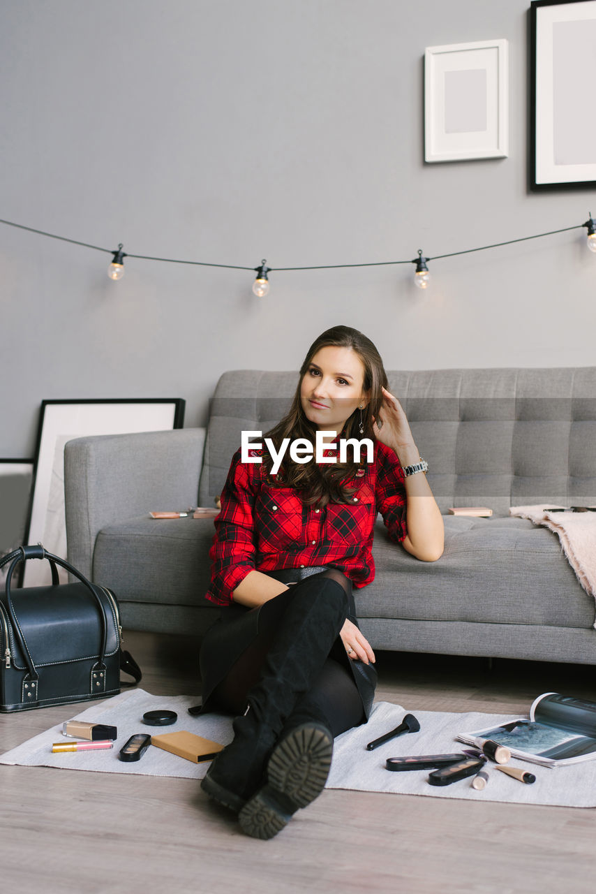 Young female makeup artist is sitting on the sofa floor next to randomly scattered brushes, makeup